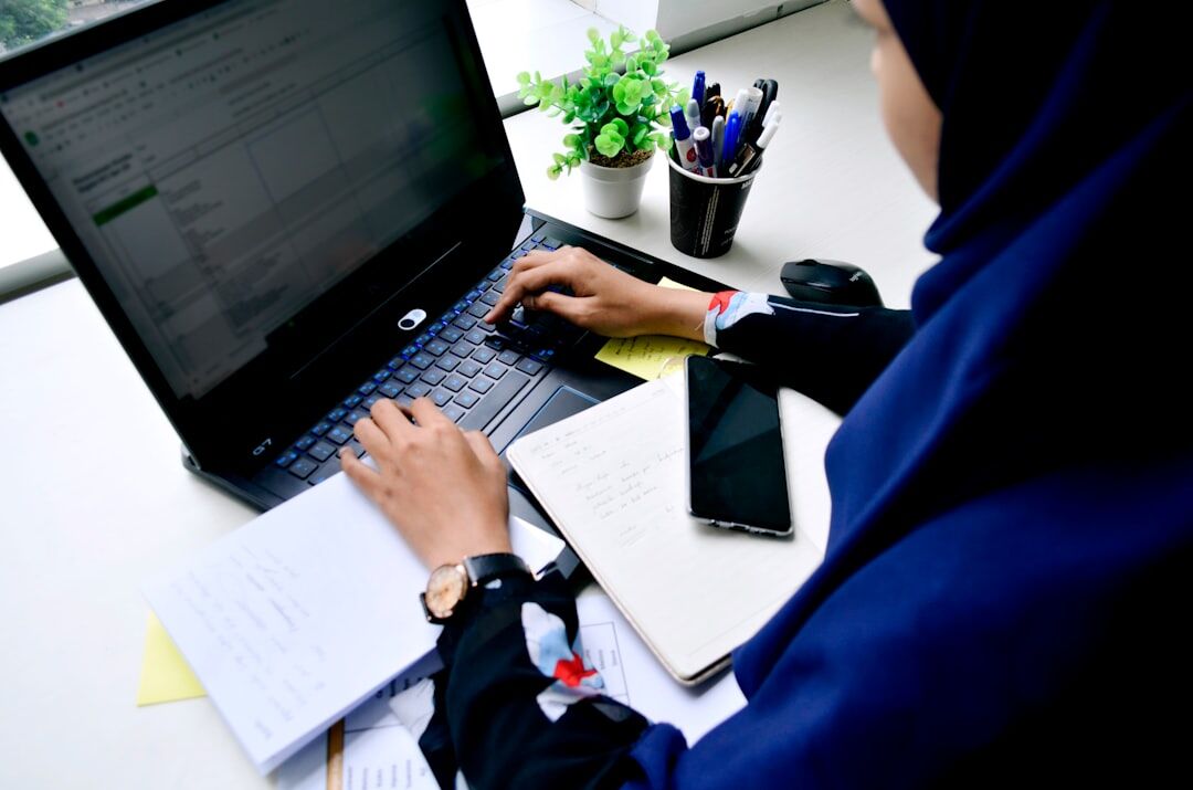 Hands writing notes in a journal next to a laptop
